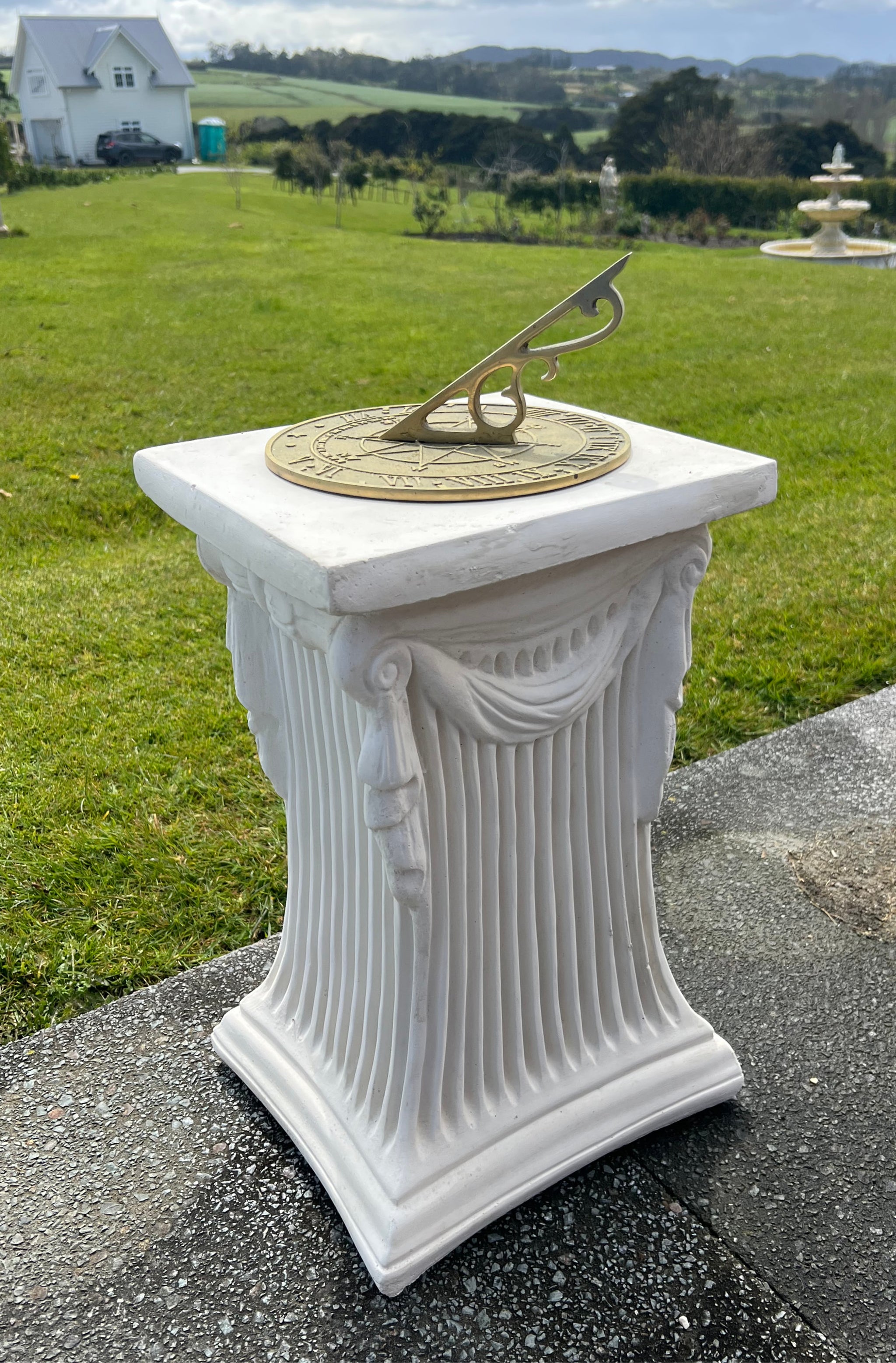 The Faraway Garden Vale Pedestal is a statement sundial with elaborate swagging and vertical moulding on all sides and showcases a detailed brass indicator.
